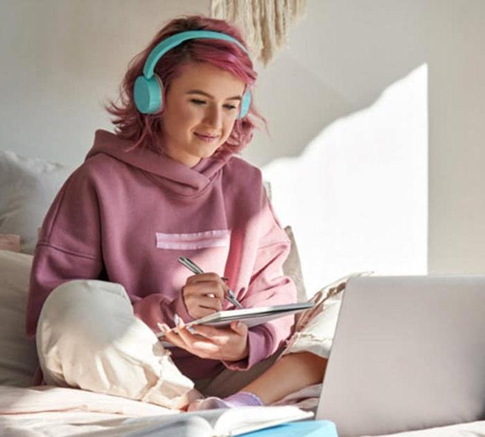 Teenage girl is sitting on her bed taking notes from her online lesson - Connections Academy